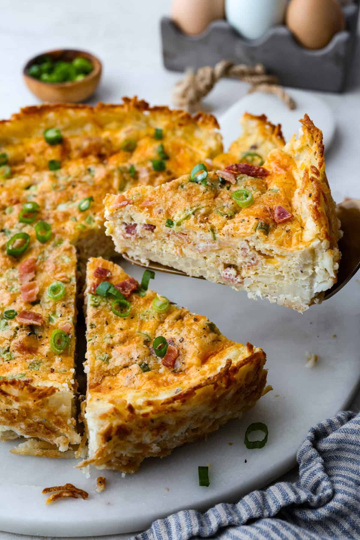 My Hash Brown Crust Quiche is a gluten-free twist on a classic! Crispy, golden potatoes wrap around a rich, savory, custardy filling. Brunch just got an upgrade! Slice of hash brown crust quiche being lifted out of the pie.