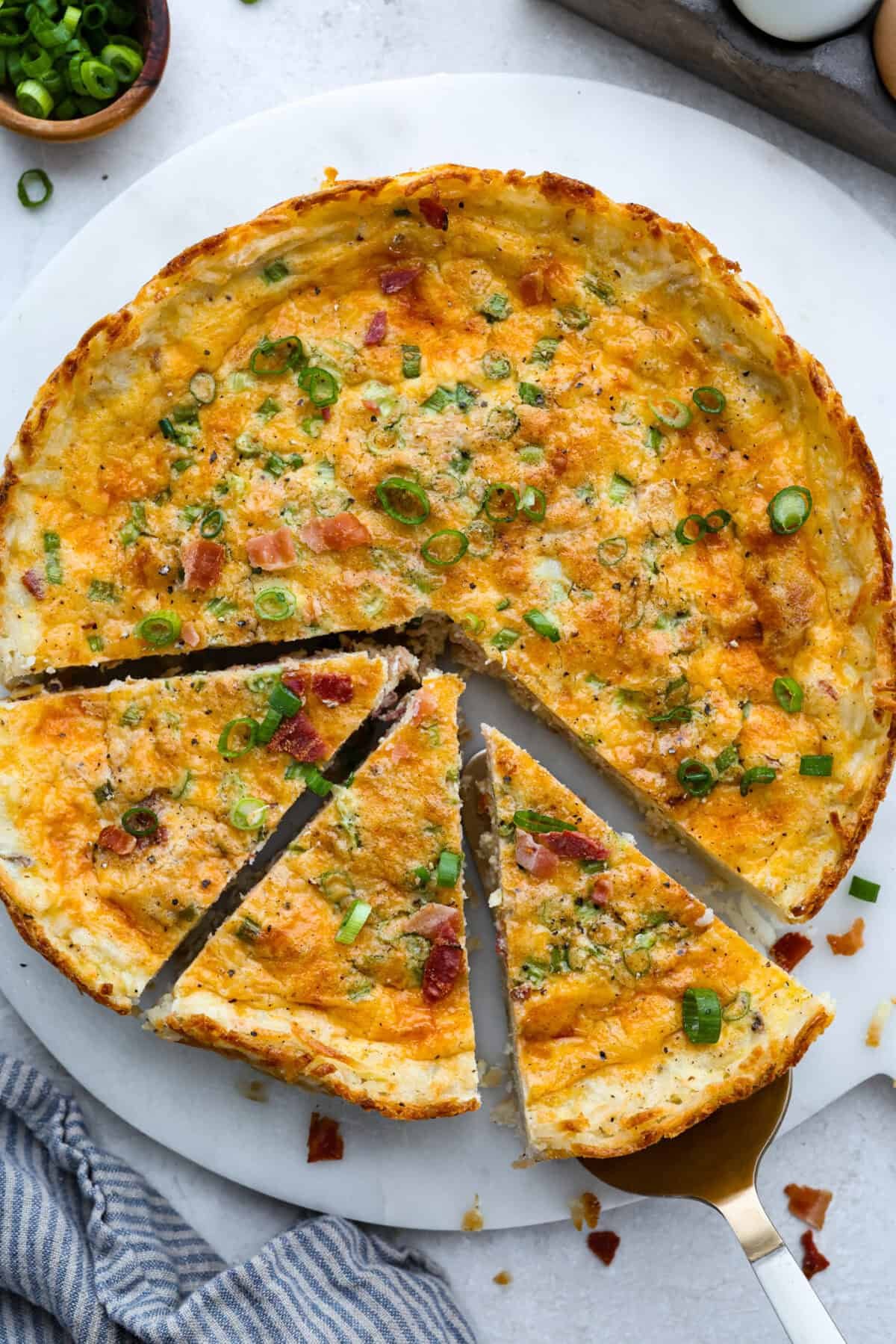 My Hash Brown Crust Quiche is a gluten-free twist on a classic! Crispy, golden potatoes wrap around a rich, savory, custardy filling. Brunch just got an upgrade! Top down shot of hash brown crust quiche on a serving platter with a few slices a little bit separated.