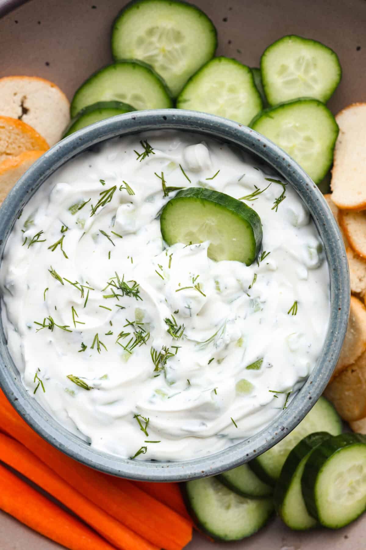 You guys are going to love how refreshing and flavorful this cucumber dip is. It's the perfect mix of creamy and crunchy and comes together in minutes! Overhead shot of cucumber dip in a bowl with veggies and crackers on the side.