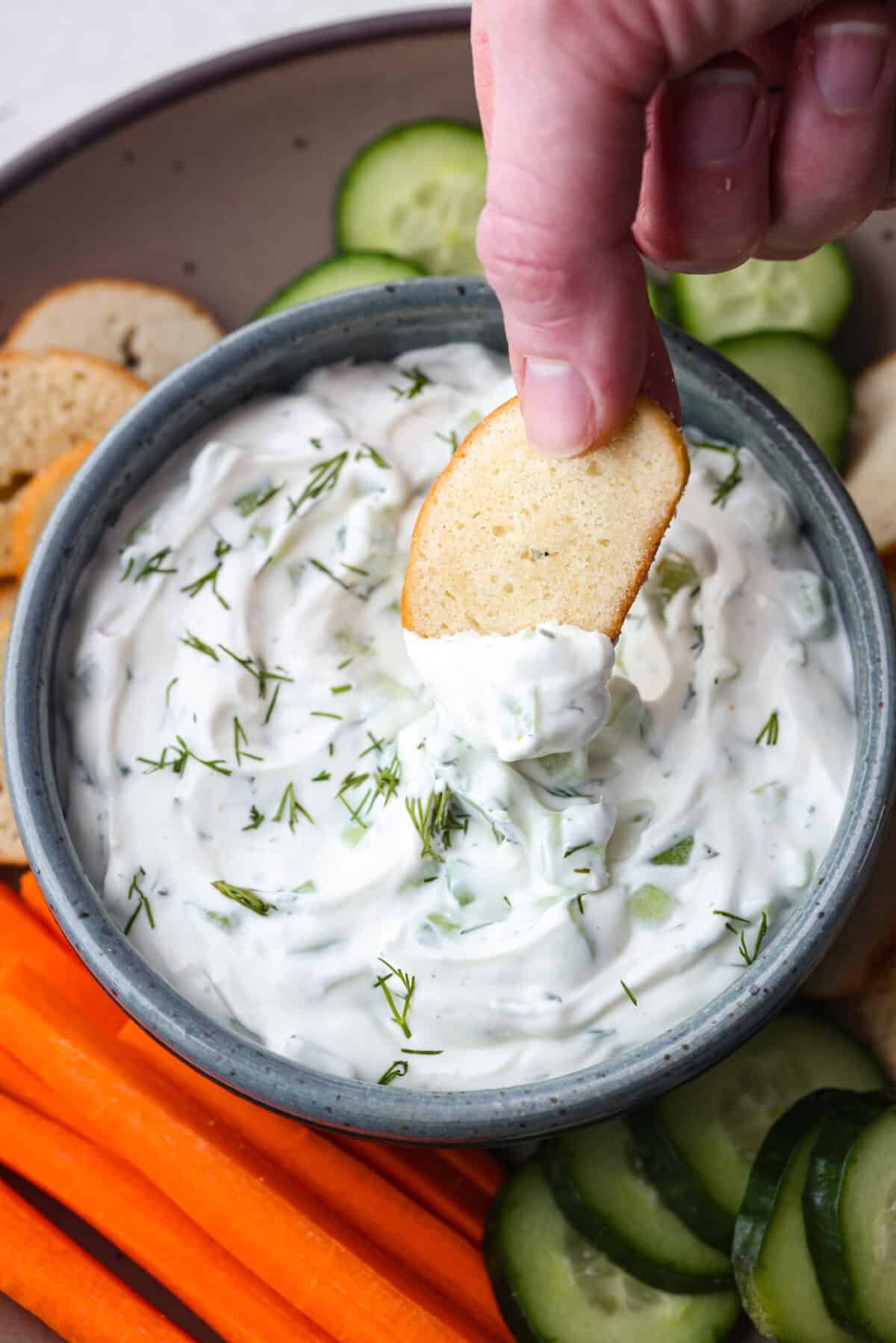 Enjoy right away, or chill for an hour to let the flavors blend and the dip thicken a bit. Close up of someone dipping a crostini into the cucumber dip.
