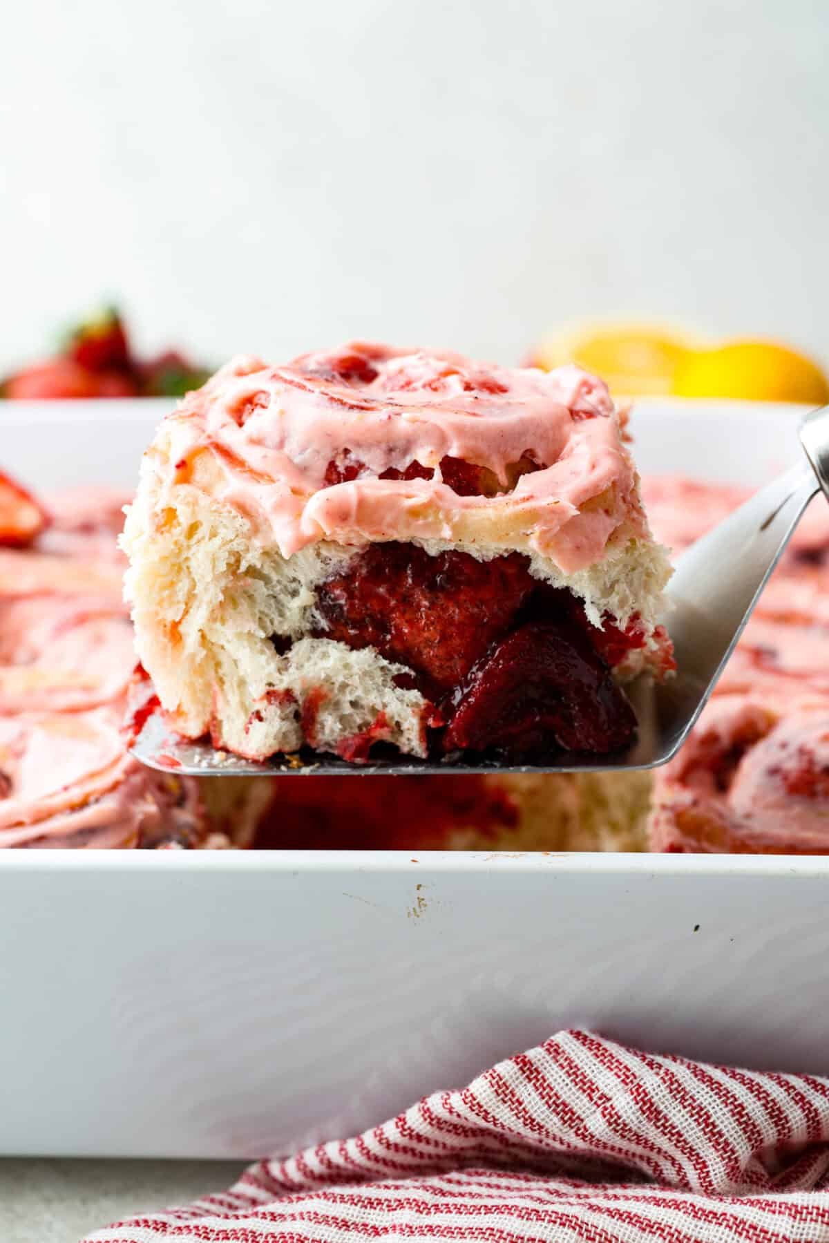 Strawberry cinnamon rolls are going to become a tradition in your house after you make these! The secret is the freeze-dried strawberries mixed with the lemon zest in the glaze - the flavor is to die for! Side shot of a strawberry cinnamon roll being lifted out of the baking dish.