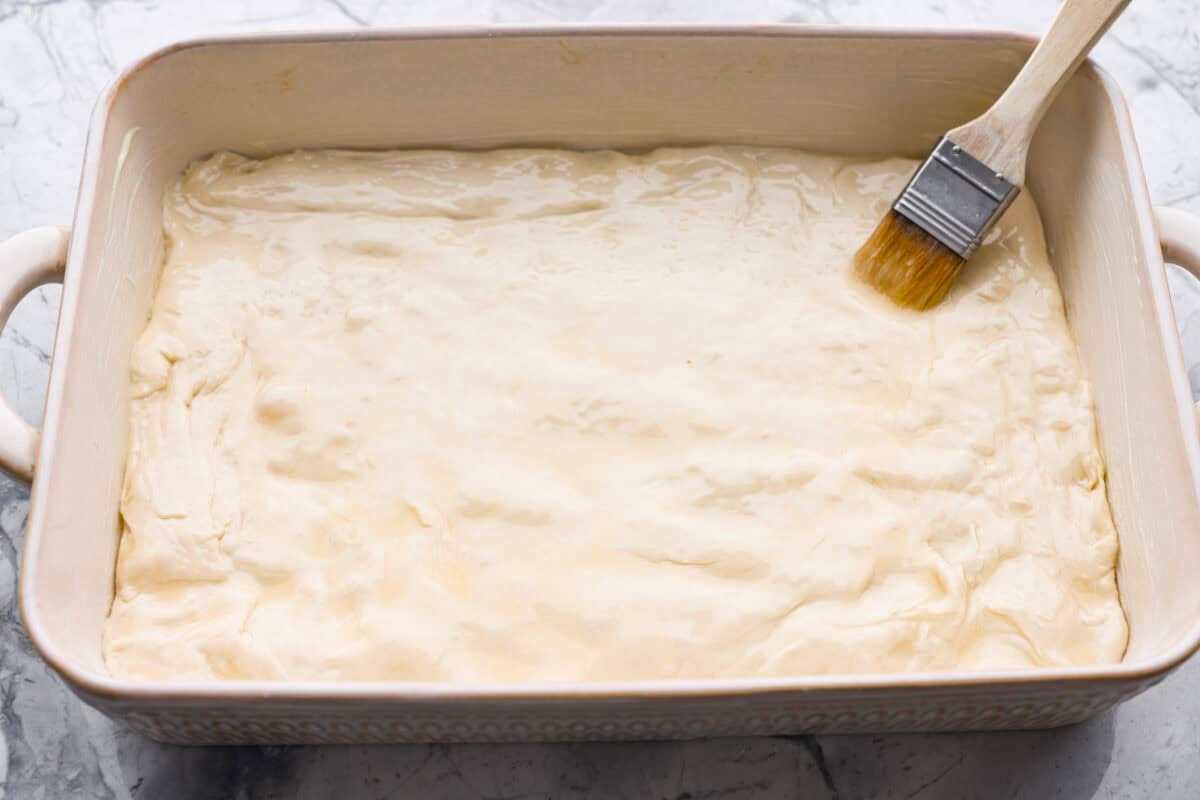 Pizza Hut breadsticks are warm, fluffy, and buttery, but this copycat recipe is even better! Coated in seasoning, parmesan, and melted butter, they’re next-level delicious. Someone brushing melted butter over the dough in a 9x13 baking dish.