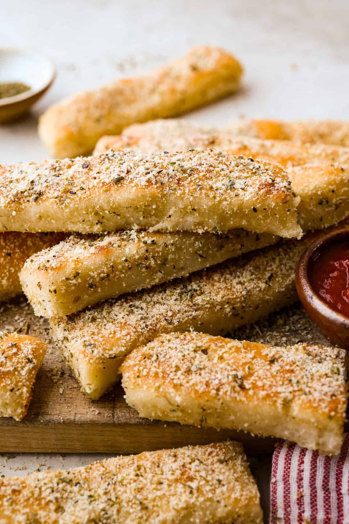 Pizza Hut breadsticks are warm, fluffy, and buttery, but this copycat recipe is even better! Coated in seasoning, parmesan, and melted butter, they’re next-level delicious. Pile of Pizza Hut breadsticks on a cutting board with a bowl of marinara sauce next to them.