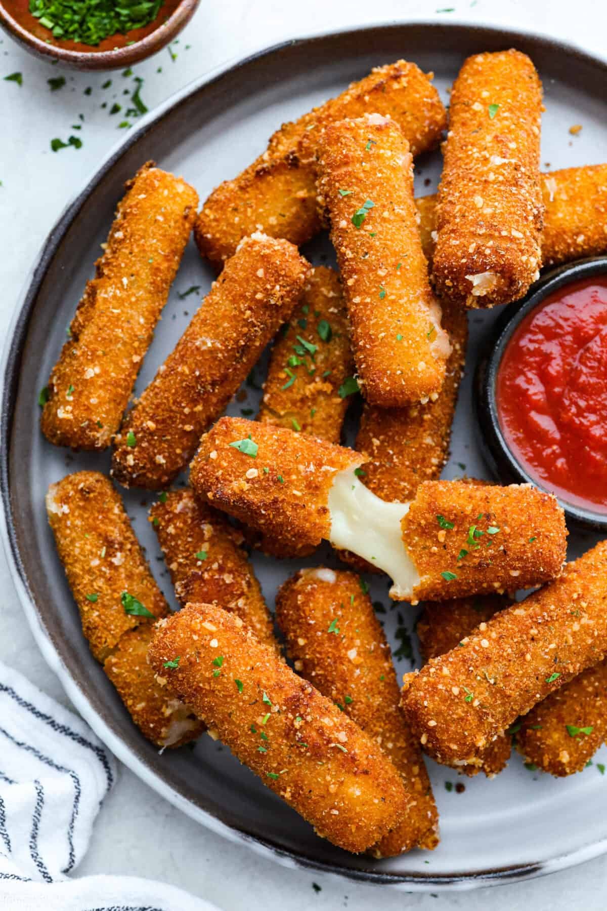 The secret to perfect mozzarella sticks comes down to three key steps: using the right mozzarella, double breading for a sturdy crust, and fully freezing them before frying. I’ve broken down these expert tips below! Overhead shot of mozzarella sticks on a serving platter with a side of marinara.
