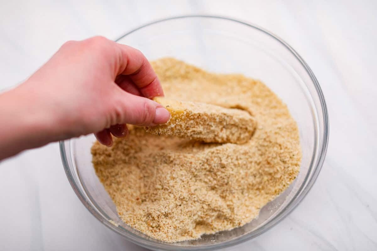 The secret to perfect mozzarella sticks comes down to three key steps: using the right mozzarella, double breading for a sturdy crust, and fully freezing them before frying. I’ve broken down these expert tips below! Someone dipping the egg dipped cheese stick into the breading mixture.