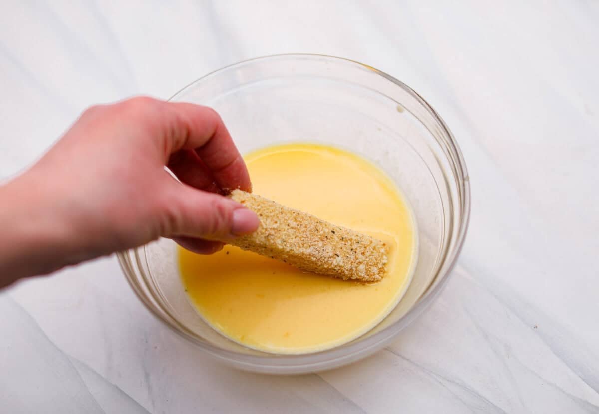 The secret to perfect mozzarella sticks comes down to three key steps: using the right mozzarella, double breading for a sturdy crust, and fully freezing them before frying. I’ve broken down these expert tips below! Someone dipping the egg and breading dipped cheese stick back into the egg mixture.