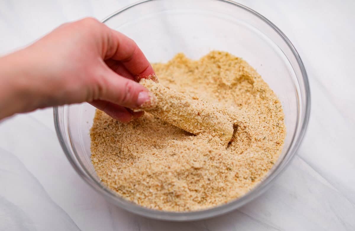 The secret to perfect mozzarella sticks comes down to three key steps: using the right mozzarella, double breading for a sturdy crust, and fully freezing them before frying. I’ve broken down these expert tips below! Someone dipping the double dipped cheese stick into the breading for a second time.