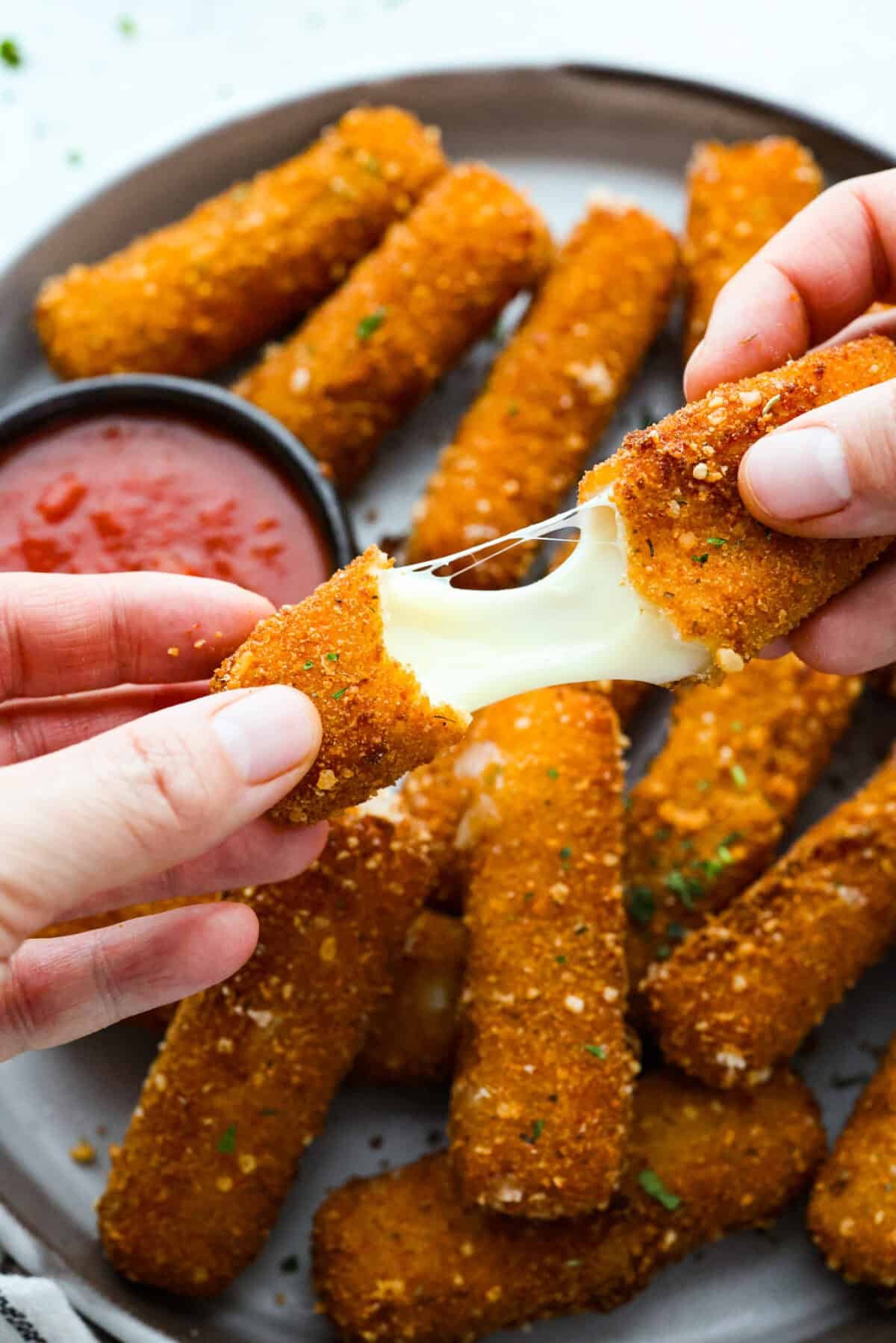 The secret to perfect mozzarella sticks comes down to three key steps: using the right mozzarella, double breading for a sturdy crust, and fully freezing them before frying. I’ve broken down these expert tips below! Close up shot of someone pulling and stretching a mozzarella stick apart.