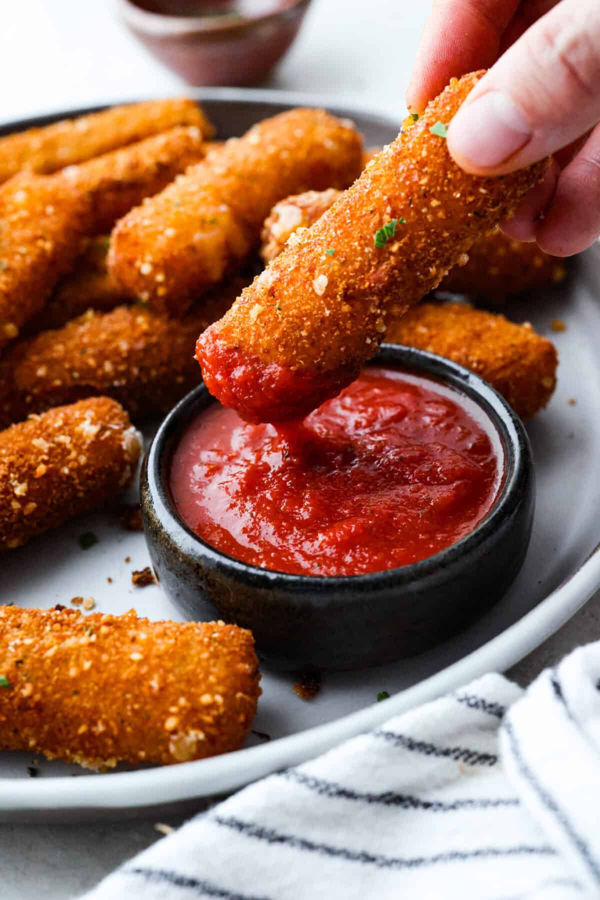 The secret to perfect mozzarella sticks comes down to three key steps: using the right mozzarella, double breading for a sturdy crust, and fully freezing them before frying. I’ve broken down these expert tips below! Someone dipping a mozzarella stick into marinara sauce.