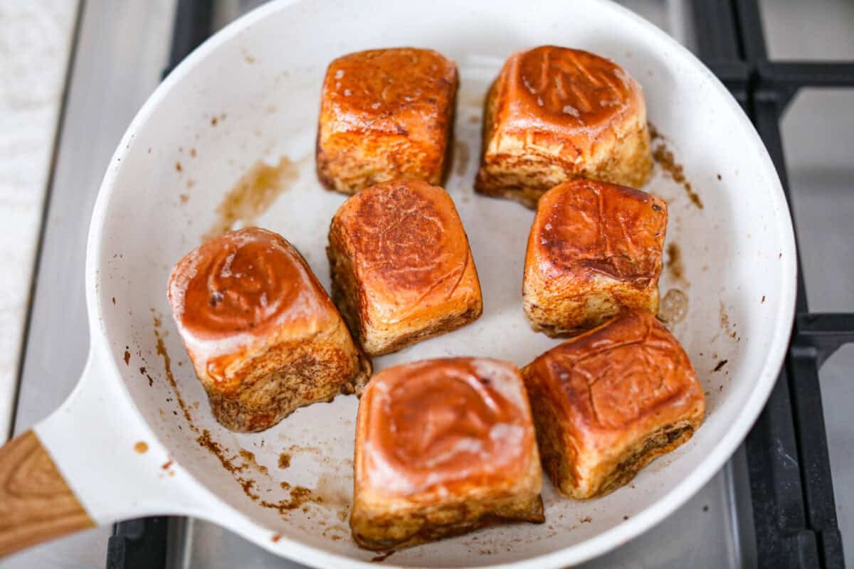 Hawaiian Roll French Toast is a fun twist on the classic, with sweet, buttery rolls that stay soft inside and turn golden outside. Instead of cutting them up, which made them too soggy, I used the whole rolls for the best texture. The real game changer was pairing them with my homemade coconut buttermilk syrup for an extra indulgent touch. Overhead shot of dipped rolls cooking in a skillet.