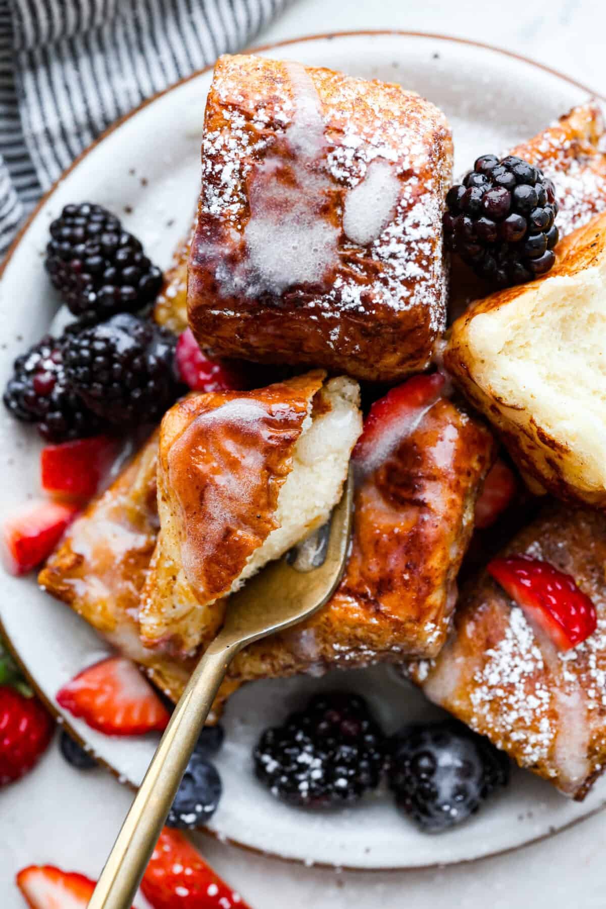 Hawaiian Roll French Toast is a fun twist on the classic, with sweet, buttery rolls that stay soft inside and turn golden outside. Instead of cutting them up, which made them too soggy, I used the whole rolls for the best texture. The real game changer was pairing them with my homemade coconut buttermilk syrup for an extra indulgent touch. Overhead shot of a plate of Hawaiian roll french toast with berries, syrup and powdered sugar.