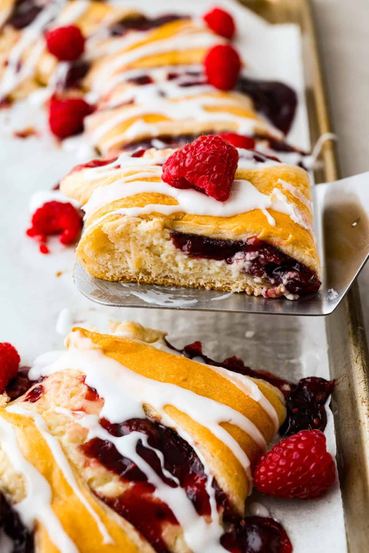 This Raspberry Cream Cheese Crescent Ring is a simple pastry with a flaky, golden crust, a sweet and tangy cream cheese filling, and a burst of raspberry flavor. Perfect for breakfast, brunch, or dessert, it's easy to make yet impressively delicious! Close up shot of a slice of raspberry cream cheese crescent ring.