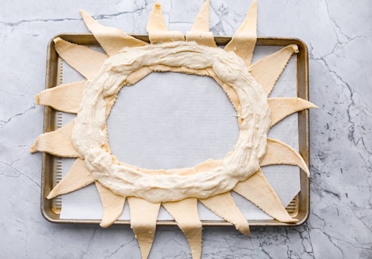 This Raspberry Cream Cheese Crescent Ring is a simple pastry with a flaky, golden crust, a sweet and tangy cream cheese filling, and a burst of raspberry flavor. Perfect for breakfast, brunch, or dessert, it's easy to make yet impressively delicious! Overhead shot of the cream cheese filling spread in a ring on the sunburst crescent rolls.