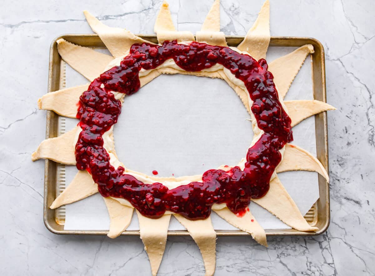 This Raspberry Cream Cheese Crescent Ring is a simple pastry with a flaky, golden crust, a sweet and tangy cream cheese filling, and a burst of raspberry flavor. Perfect for breakfast, brunch, or dessert, it's easy to make yet impressively delicious! Overhead shot of the raspberry filling spread over the cream cheese and crescent rolls.