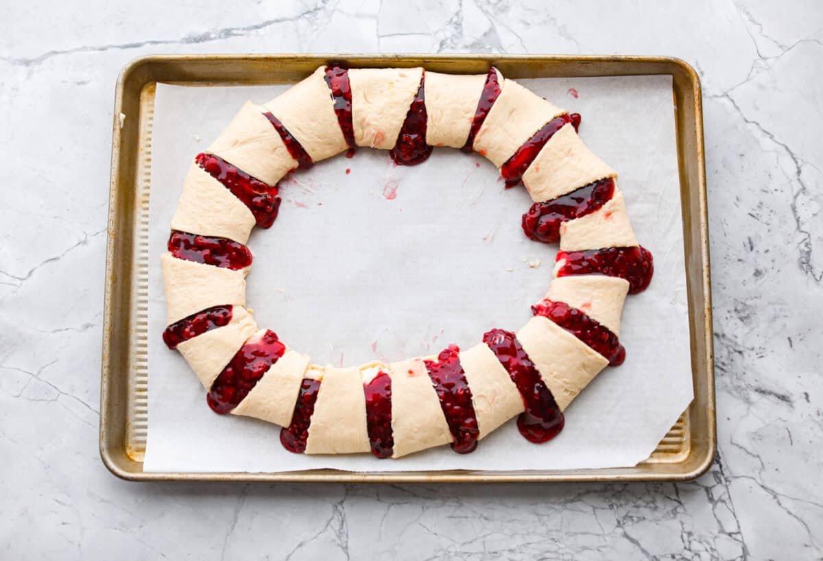 This Raspberry Cream Cheese Crescent Ring is a simple pastry with a flaky, golden crust, a sweet and tangy cream cheese filling, and a burst of raspberry flavor. Perfect for breakfast, brunch, or dessert, it's easy to make yet impressively delicious! Overhead shot of the crescent rolls wrapped around the top of the raspberry and cream cheese filling to make a ring.