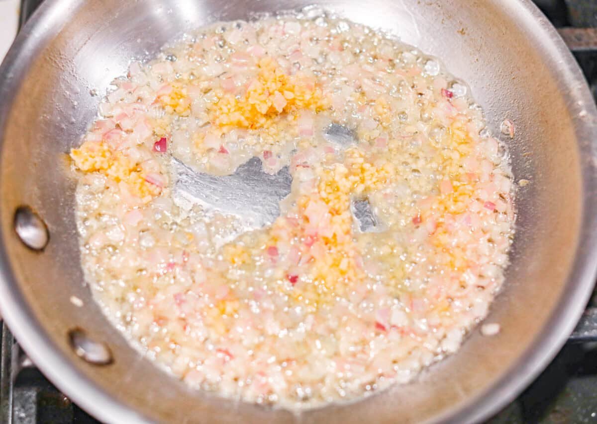 These Crab Stuffed Mushrooms are a deliciously savory appetizer, perfect for impressing guests at any gathering. With a rich crab filling in every bite, they’re sure to be a crowd favorite! Overhead shot of garlic and shallots cooking in butter in a skillet.