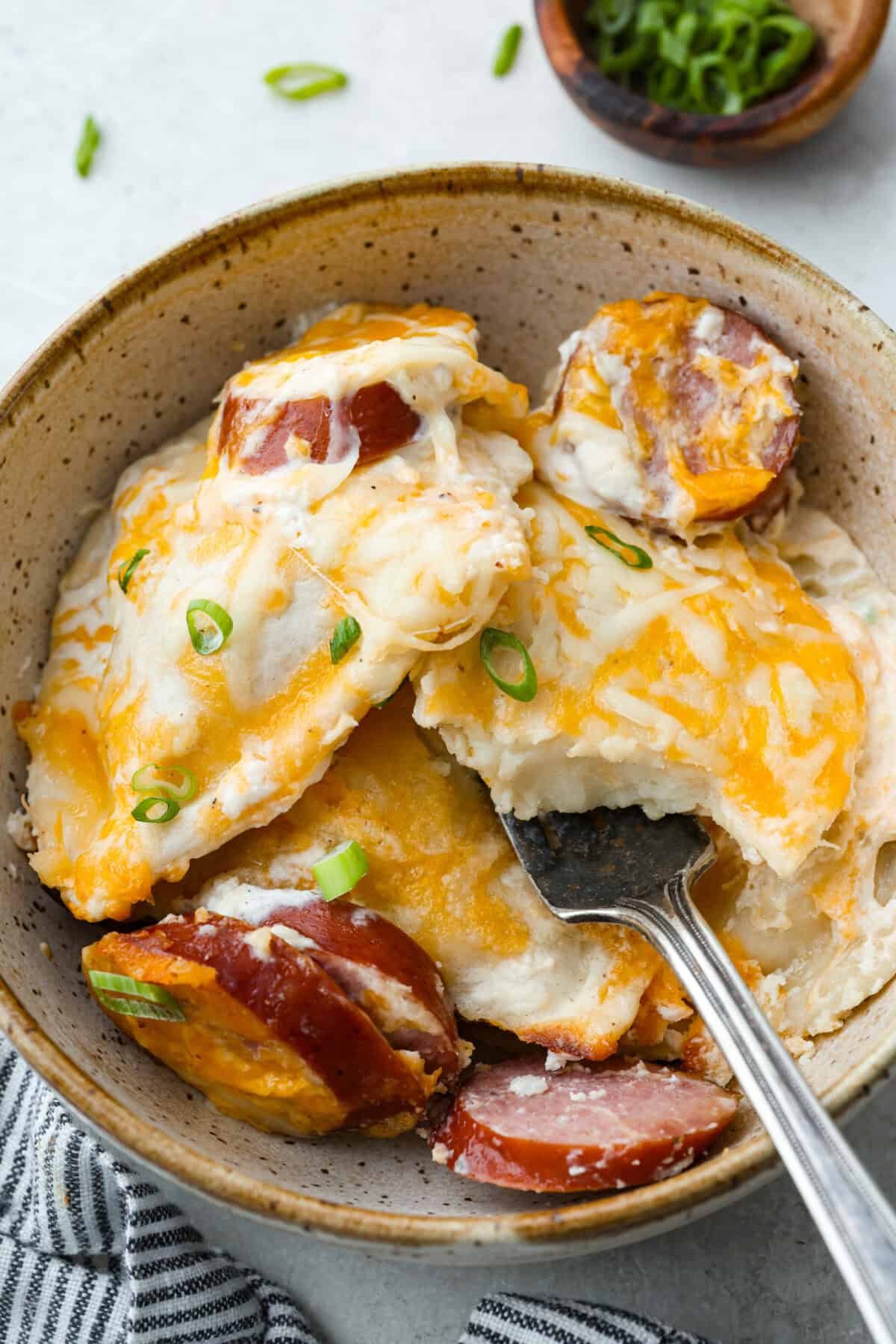 This isn’t your average Pierogi Casserole. While most stick to one type of cheese, I use a blend for ooey-gooey cheesy creaminess and cozy flavor in every bite. A bowl of pierogi casserole with kielbasa and a fork.