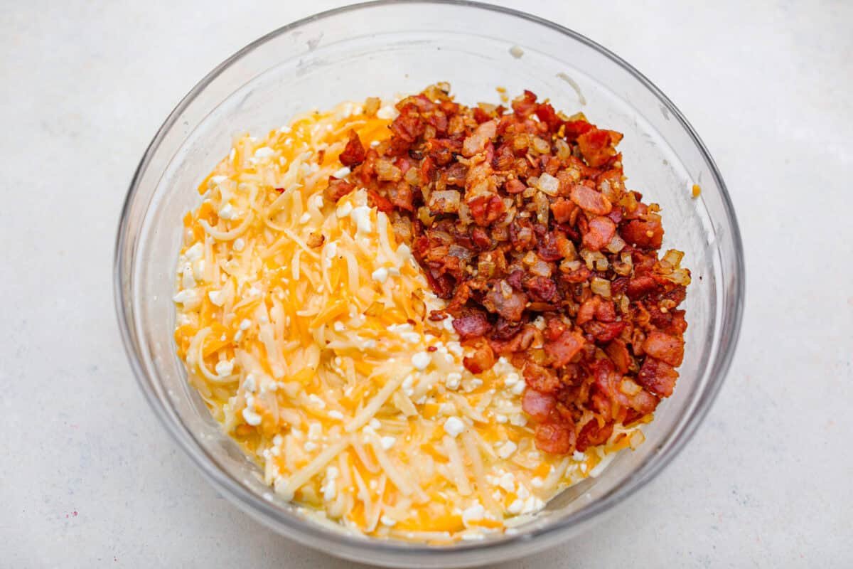 Kickstart your day with this hearty Amish Breakfast Casserole! It's loaded with crispy bacon, tender hash browns, and gooey melted cheese. This dish is a crowd-pleaser that’s perfect for family breakfasts and holiday mornings! Overhead shot of the cheese and potato mixture with bacon and onion mixture in a bowl.