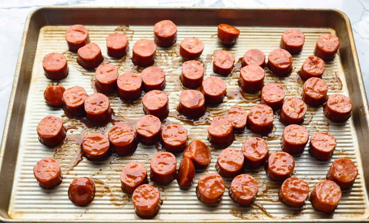 Kielbasa Bites are the ultimate crowd-pleasing appetizer! With their smoky, savory flavor and caramelized glaze sweetness, these bite-sized snacks are easy to make and always a hit at parties, game days, or anytime you need a quick appetizer! Overhead shot of glazed kielbasa slices spread out on a baking sheet.