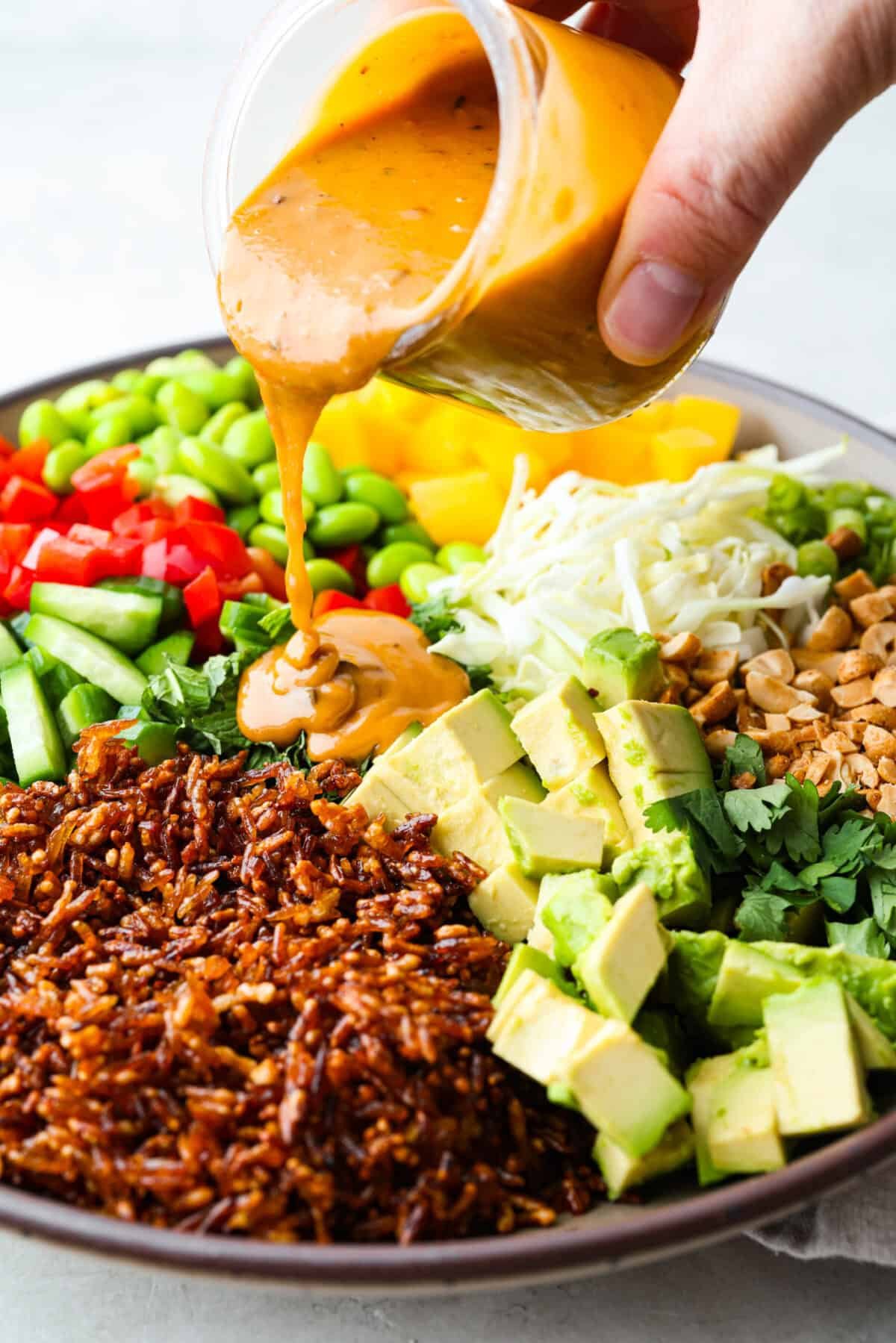 This trendy Crispy rice salad is a perfect mix of crunch, freshness, and bold flavor! Golden rice, vibrant veggies, and a creamy dressing make every bite irresistible. Someone drizzling the dressing over the crispy rice salad.