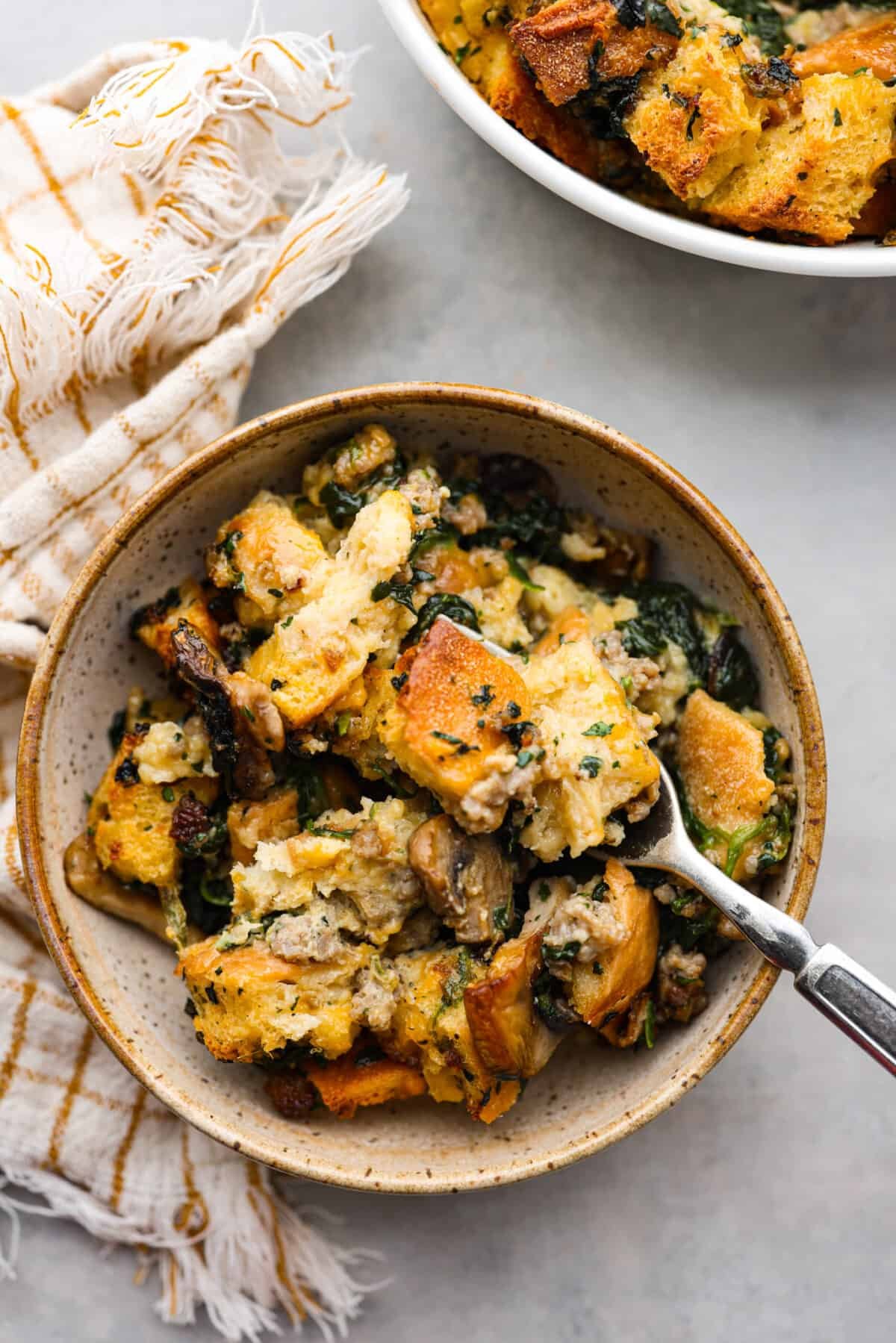 This breakfast strata is bursting with savory sausage, tender mushrooms, soft bread pieces, and melty cheddar. Perfect for your next holiday or family breakfast. It is packed with so much delicious flavor and texture that it will leave you wanting seconds! Overhead shot of plated breakfast strata.