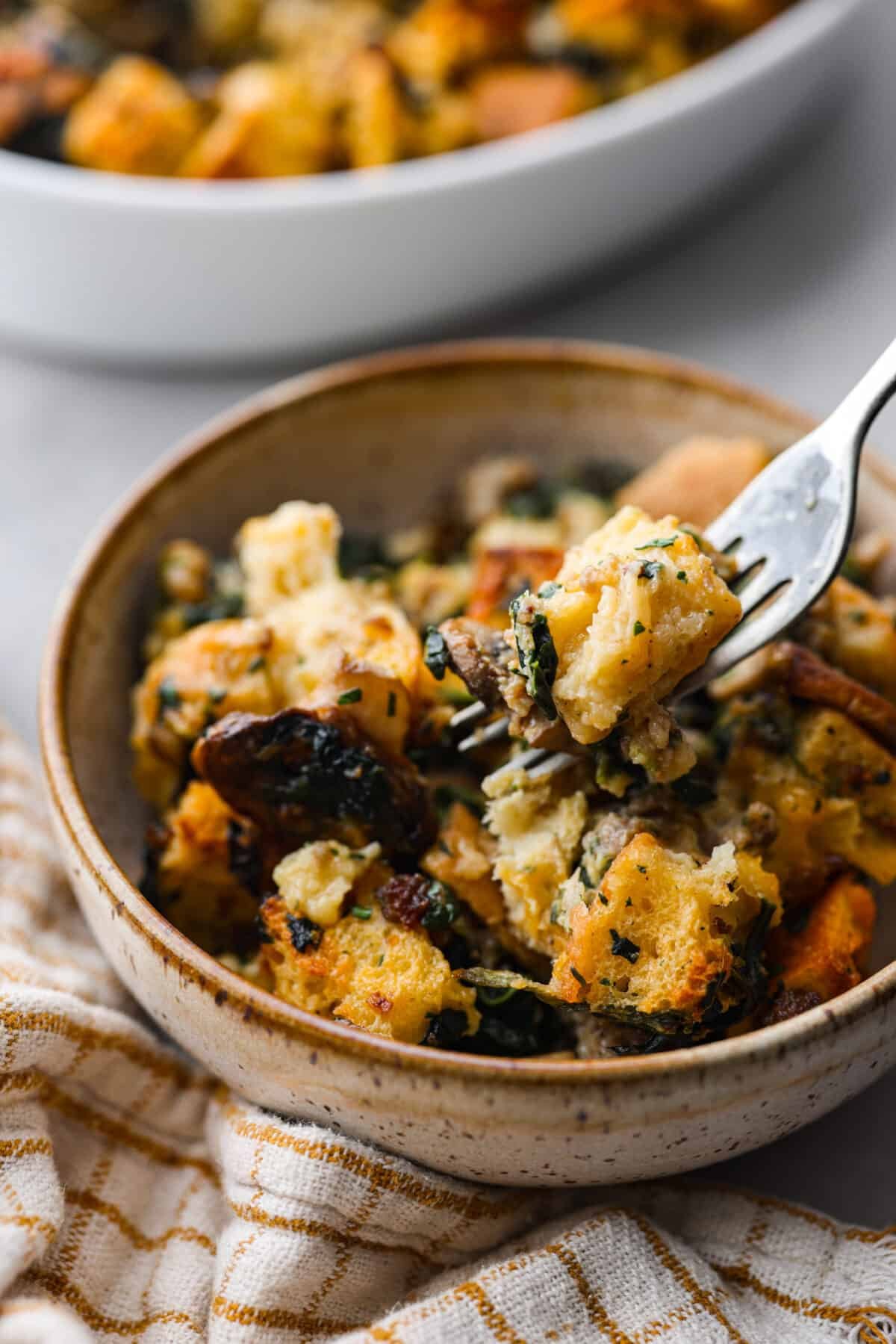 This breakfast strata is bursting with savory sausage, tender mushrooms, soft bread pieces, and melty cheddar. Perfect for your next holiday or family breakfast. It is packed with so much delicious flavor and texture that it will leave you wanting seconds! Angle shot of plated breakfast strata in a bowl.