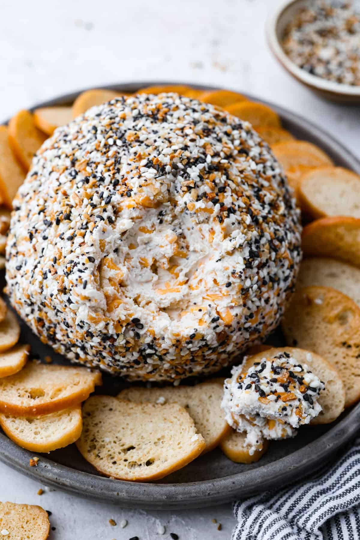 This everything bagel cheese ball combines the creamy richness of cheese with the savory blend of everything bagel seasoning! It's an irresistible appetizer you can serve with crackers, bagel chips, or veggies! Everyone will love it! Angle shot of an everything bagel cheese ball on a platter.