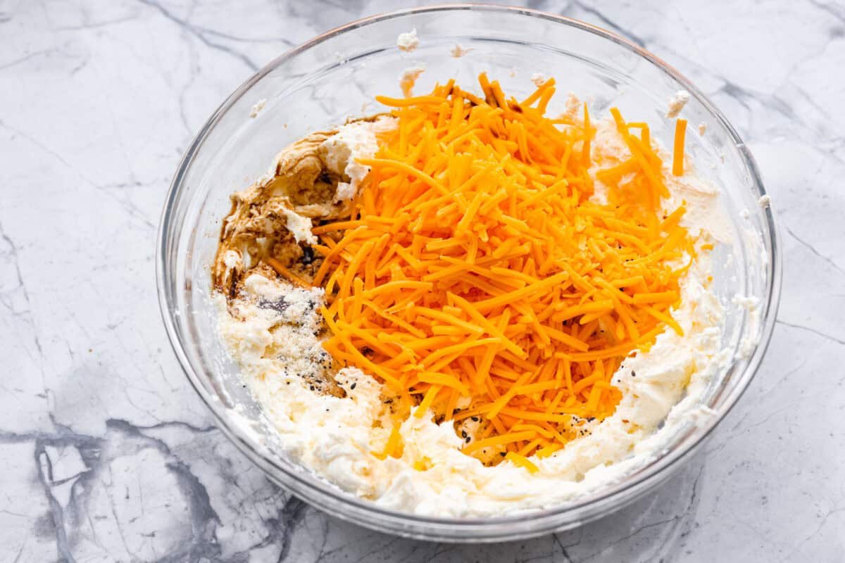 This everything bagel cheese ball combines the creamy richness of cheese with the savory blend of everything bagel seasoning! It's an irresistible appetizer you can serve with crackers, bagel chips, or veggies! Everyone will love it! Overhead shot of the cream cheese with cheddar cheese, garlic powder, onion powder, Worcestershire sauce and seasoning in a bowl.