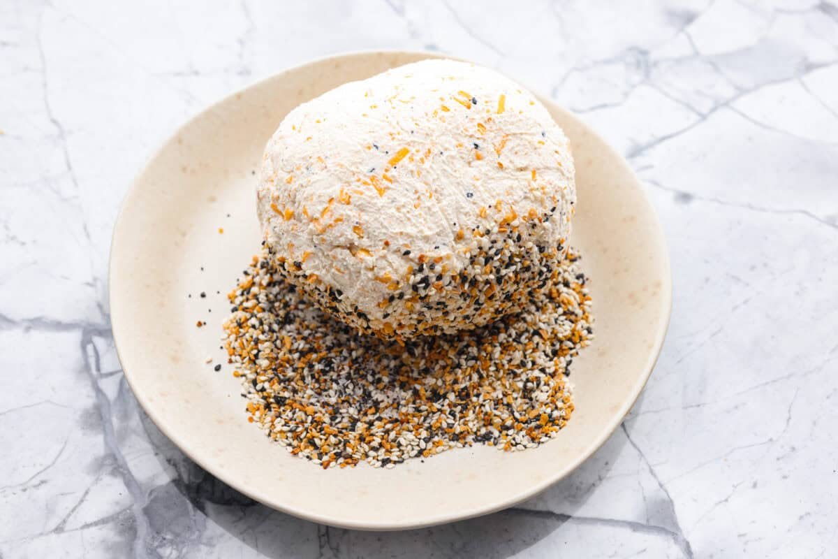 This everything bagel cheese ball combines the creamy richness of cheese with the savory blend of everything bagel seasoning! It's an irresistible appetizer you can serve with crackers, bagel chips, or veggies! Everyone will love it! Overhead shot of the ball being rolled in everything bagel seasoning.