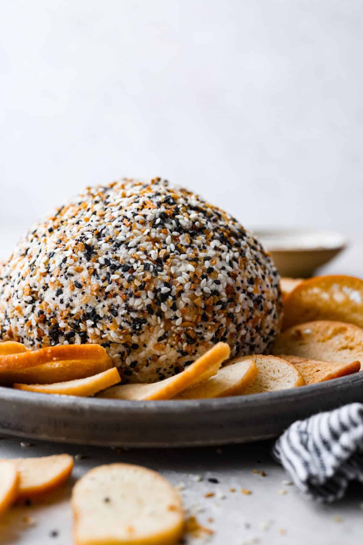 This everything bagel cheese ball combines the creamy richness of cheese with the savory blend of everything bagel seasoning! It's an irresistible appetizer you can serve with crackers, bagel chips, or veggies! Everyone will love it! Side shot of the everything bagel cheese ball on a platter.