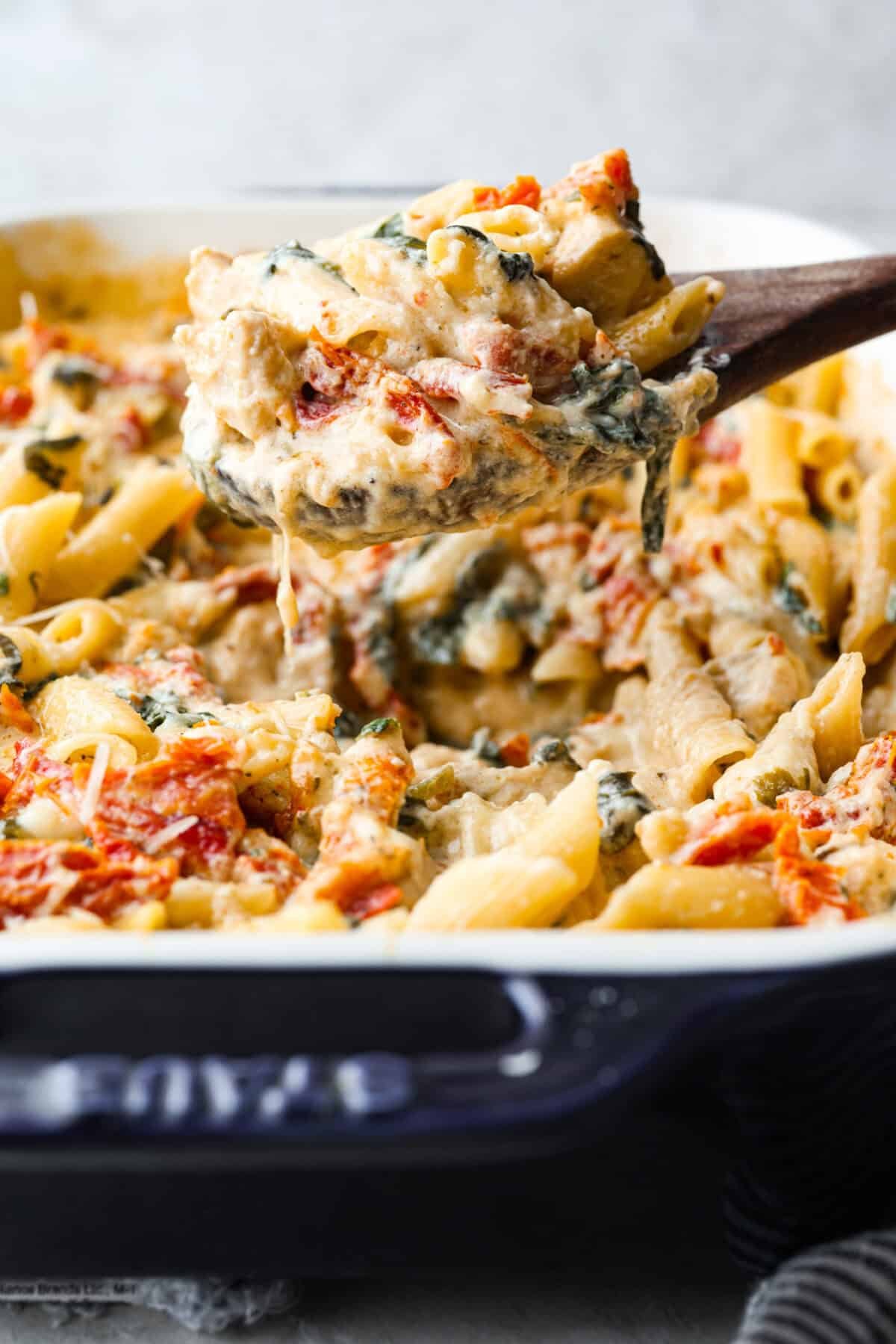 You all love my Crockpot Tuscan Chicken, and I know casseroles are a favorite as well. So, I combined them into this irresistibly delicious Tuscan Chicken Casserole! Shot of some one lifting a portion of tuscan chicken casserole out of the baking dish.