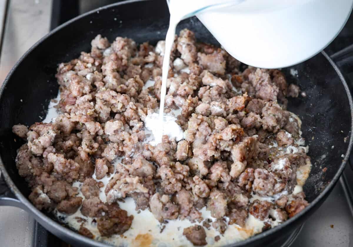 Homemade sausage gravy is perfect for a comforting breakfast! In just 15 minutes and with a few simple ingredients, you’ll have a delicious, hearty gravy to top fluffy biscuits. Angle shot of someone pouring half and half into a large skillet with the meat and flour mixture.