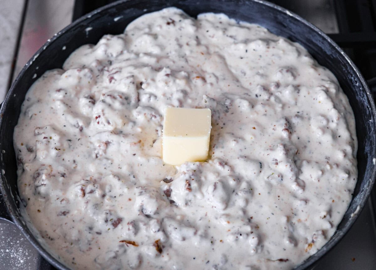 Homemade sausage gravy is perfect for a comforting breakfast! In just 15 minutes and with a few simple ingredients, you’ll have a delicious, hearty gravy to top fluffy biscuits. Overhead shot of the creamy gravy and meat mixture with a cube of butter in the middle.