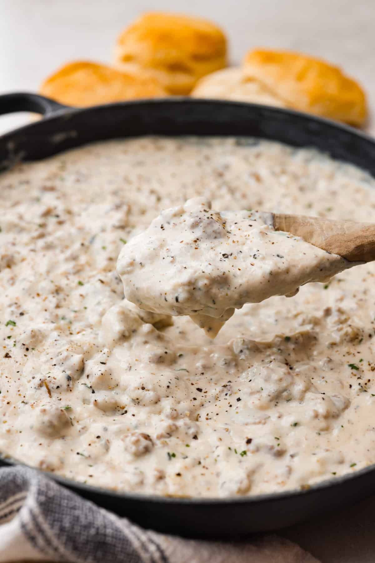 Homemade sausage gravy is perfect for a comforting breakfast! In just 15 minutes and with a few simple ingredients, you’ll have a delicious, hearty gravy to top fluffy biscuits. Close up shot of sausage gravy in a skillet with someone scooping some out with a wooden spoon.