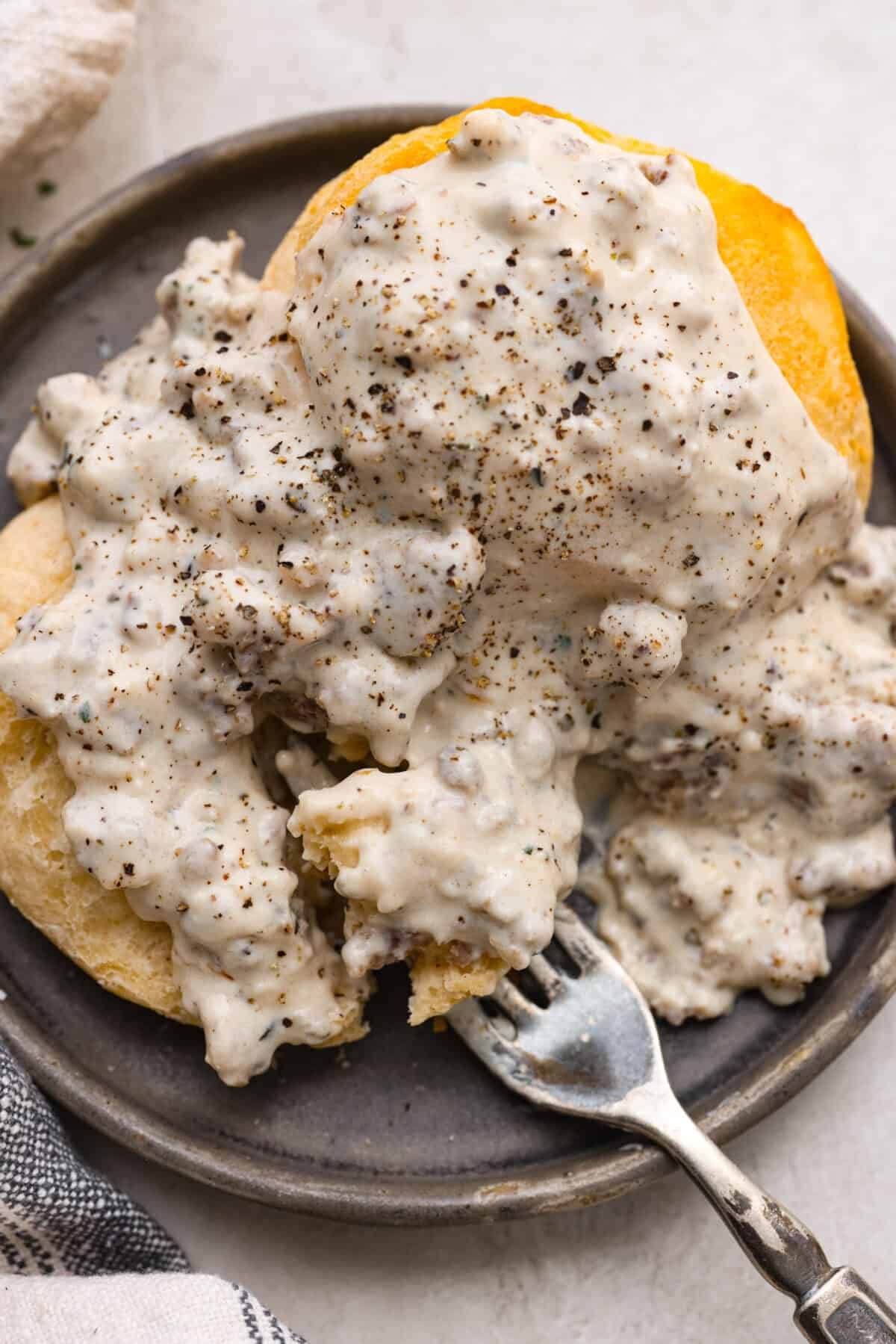 Homemade sausage gravy is perfect for a comforting breakfast! In just 15 minutes and with a few simple ingredients, you’ll have a delicious, hearty gravy to top fluffy biscuits. Overhead shot of sausage gravy over a fluffy biscuit on a plate.