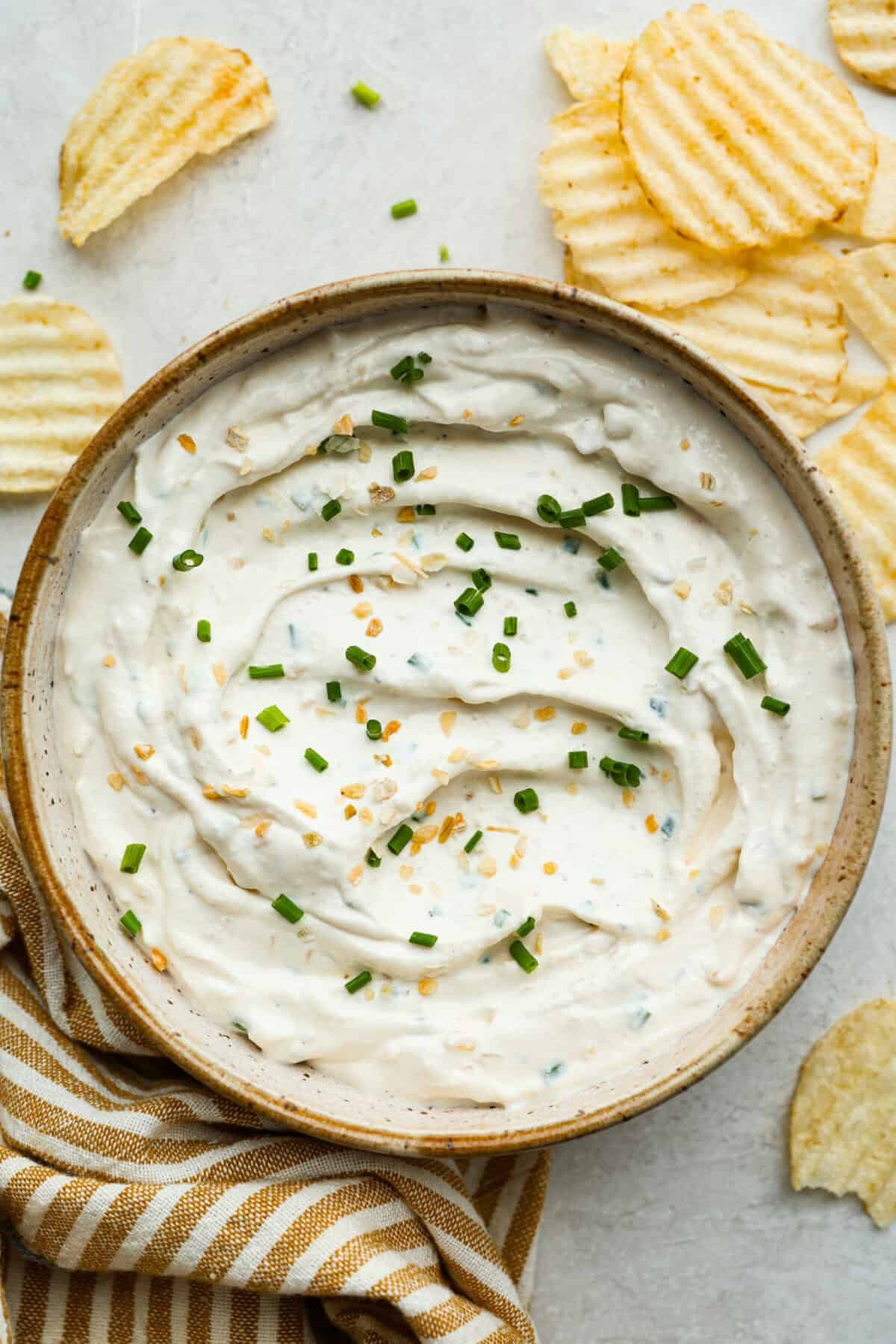 This sour cream and onion dip has become a staple at all of our family get togethers. It's the perfect appetizer, even the kids cant get enough! The rich and creamy dip is packed with incredible onion flavor. Overhead shot of sour cream and onion dip in a bowl with wavy chips around it.