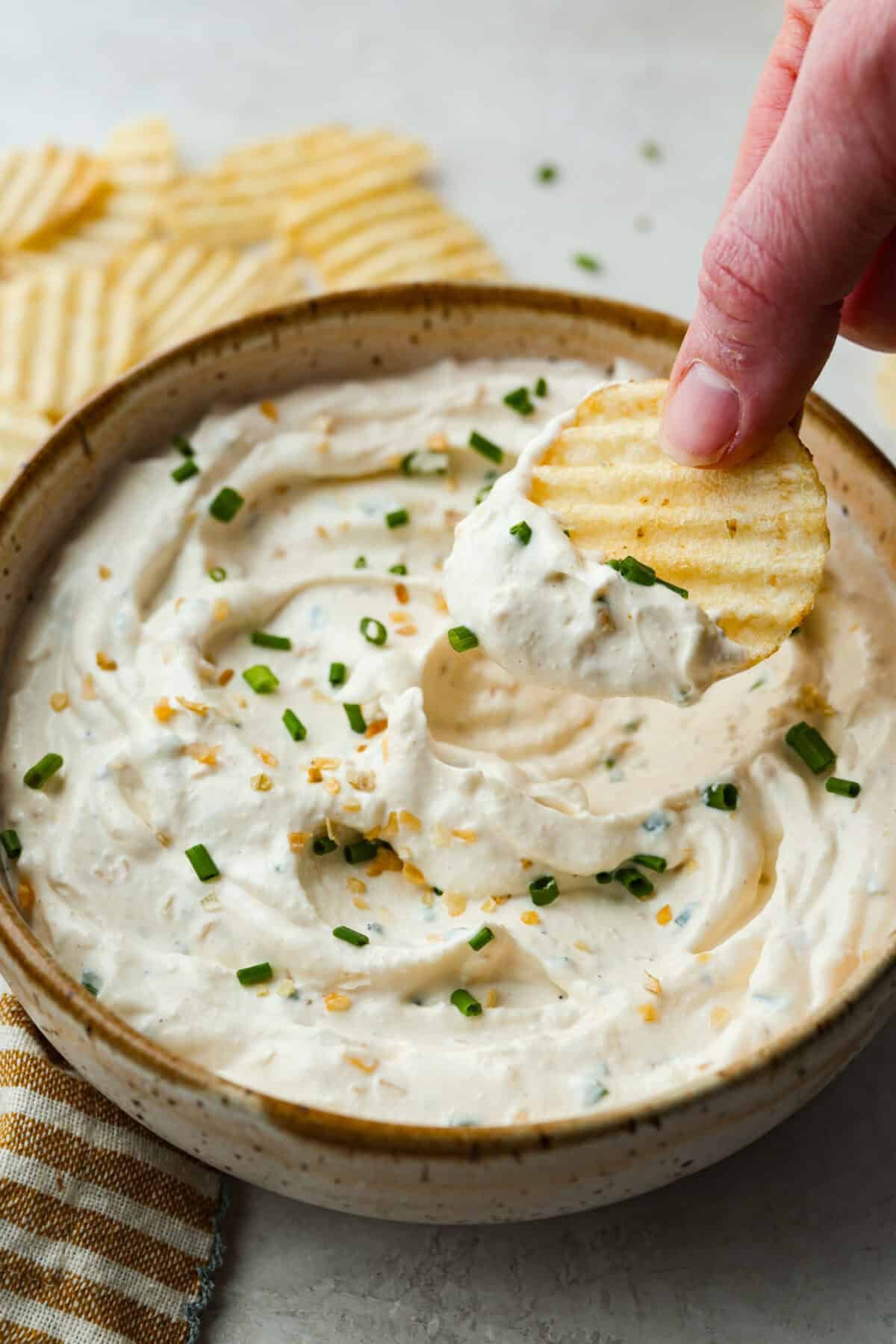 This sour cream and onion dip has become a staple at all of our family get togethers. It's the perfect appetizer, even the kids cant get enough! The rich and creamy dip is packed with incredible onion flavor. Close up shot of someone scooping a bite of sour cream and onion dip with a chip.