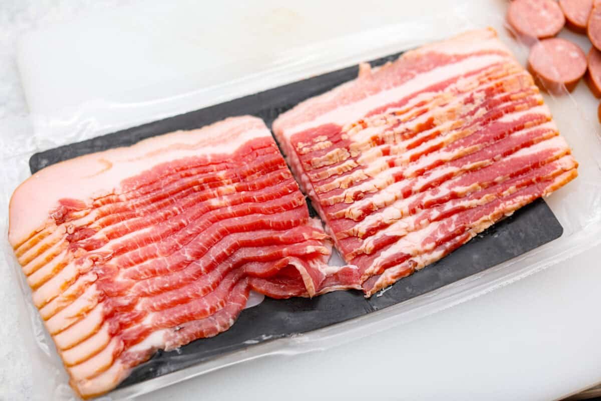 Get ready to wow your taste buds with Pig Shots! These bite-sized creations feature smoky bacon wrapped around savory sausage, filled with a creamy, flavorful cream cheese mixture. Shaped like mini shot glasses, they’re the perfect snack for game day, parties, or anytime you're looking for a unique appetizer. Overhead shot of a pack of thick cut bacon cut in half.