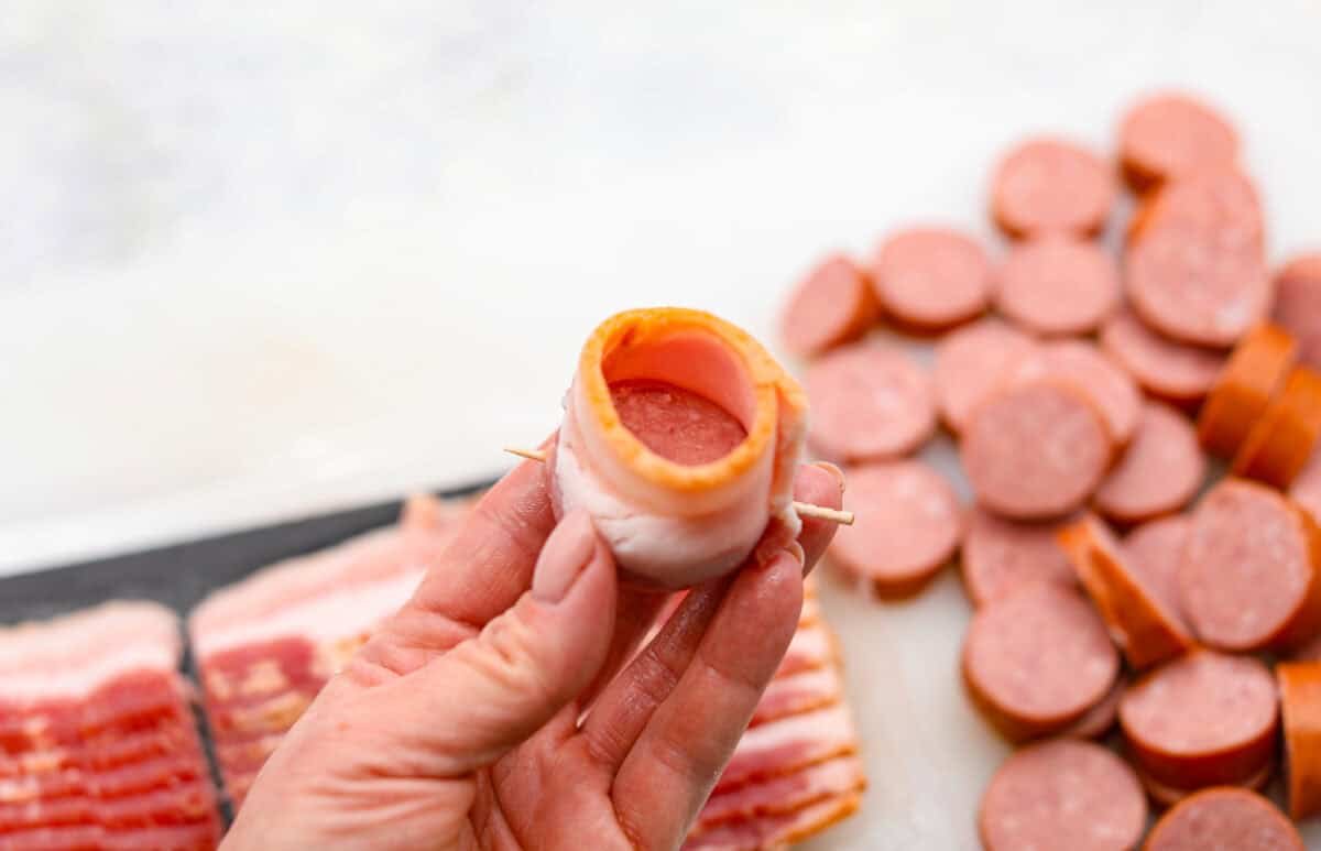 Get ready to wow your taste buds with Pig Shots! These bite-sized creations feature smoky bacon wrapped around savory sausage, filled with a creamy, flavorful cream cheese mixture. Shaped like mini shot glasses, they’re the perfect snack for game day, parties, or anytime you're looking for a unique appetizer. Angle shot of a sausage slice wrapped in bacon with a toothpick sticking through it.