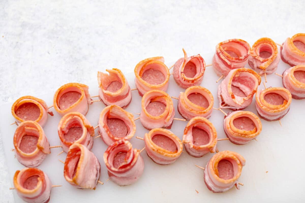 Get ready to wow your taste buds with Pig Shots! These bite-sized creations feature smoky bacon wrapped around savory sausage, filled with a creamy, flavorful cream cheese mixture. Shaped like mini shot glasses, they’re the perfect snack for game day, parties, or anytime you're looking for a unique appetizer. Overhead shot of all of the slices of sausage wrapped in bacon.
