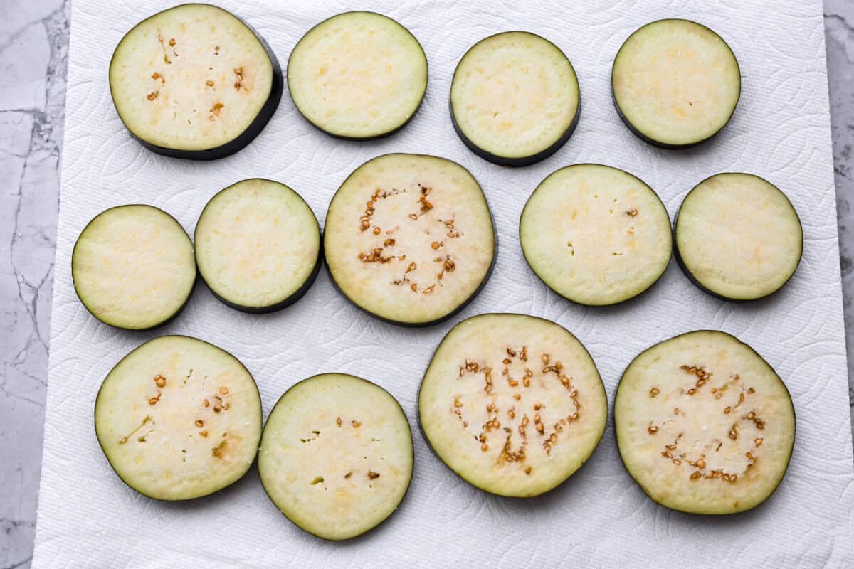 Crispy Air Fryer Eggplant is a fun flavor snack that is a healthier option than typical fried snacks. Tender eggplant slices are coated in crispy breadcrumbs and parmesan cheese, deliciously seasoned, then air-fried to perfection. Overhead shot of sliced eggplant on paper towels.