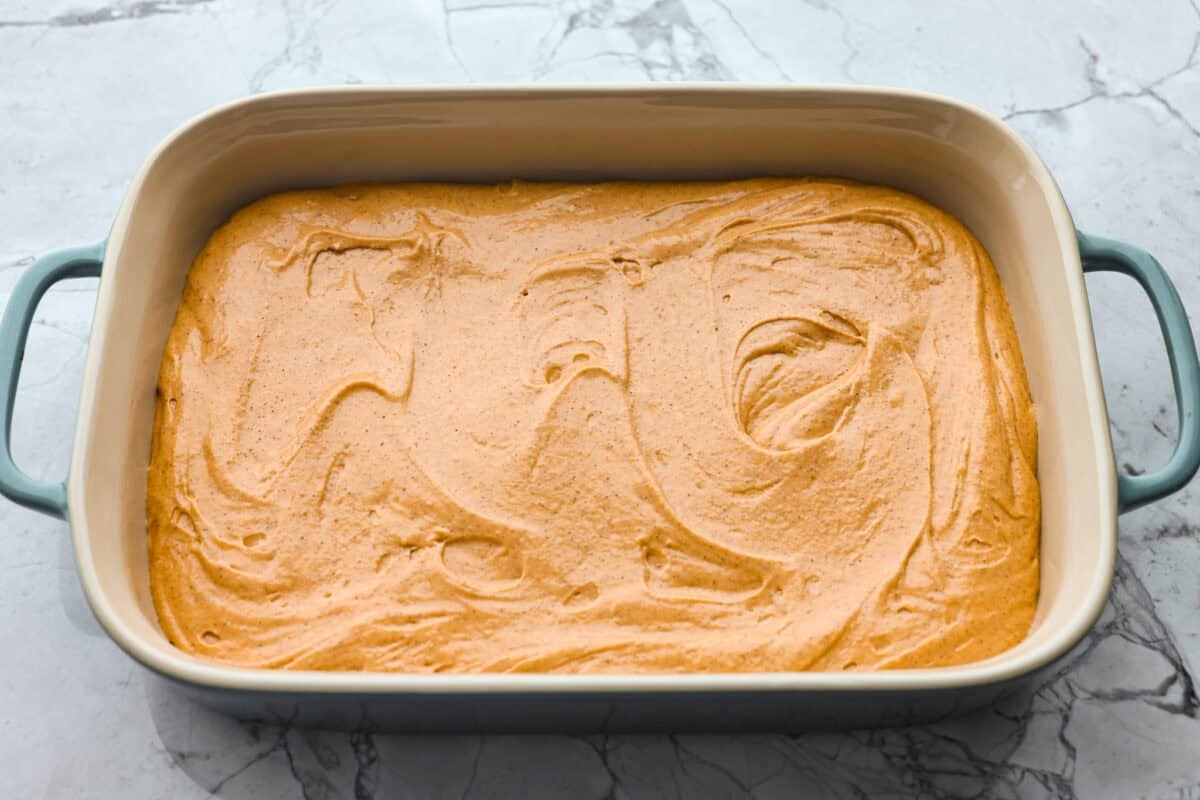 It's time to bring back the retro Tomato Soup Cake! In 1960, it was the first recipe to appear on a soup label. It resembles a moist and delicious spice cake topped with cream cheese frosting. I know you're skeptical, but trust me, it will knock your socks off! Tomato soup cake batter spread out in a baking dish.