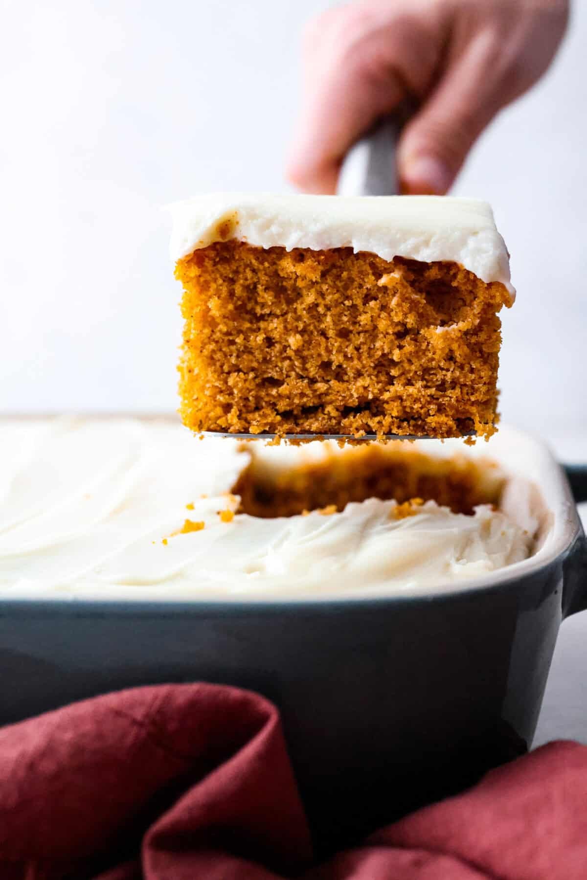 It's time to bring back the retro Tomato Soup Cake! In 1960, it was the first recipe to appear on a soup label. It resembles a moist and delicious spice cake topped with cream cheese frosting. I know you're skeptical, but trust me, it will knock your socks off! Side shot of someone lifting a piece of tomato soup cake out of the baking dish.