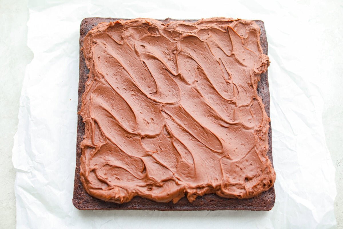 Rich, fudgy, and packed with deep chocolate flavor, Guinness Brownies are a must-try for any dessert lover! The stout beer enhances the cocoa, adding a subtle, malty depth of flavor that makes these brownies rich and irresistibly delicious. Overhead shot of baked and frosted Guinness brownies on a piece of parchment paper.
