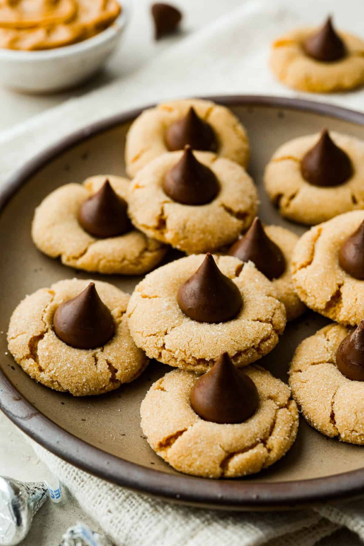 Peanut Butter Blossom Cookies are classic cookies that are perfect for every occasion. The delicious pairing of peanut butter and chocolate in these soft, buttery cookies will delight cookie lovers of all ages. Angle shot of peanut butter blossom cookies on a serving platter.