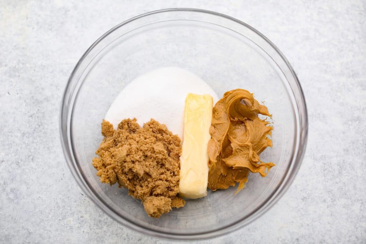 Peanut Butter Blossom Cookies are classic cookies that are perfect for every occasion. The delicious pairing of peanut butter and chocolate in these soft, buttery cookies will delight cookie lovers of all ages. Overhead shot of the sugars, butter and peanut butter in a bowl.