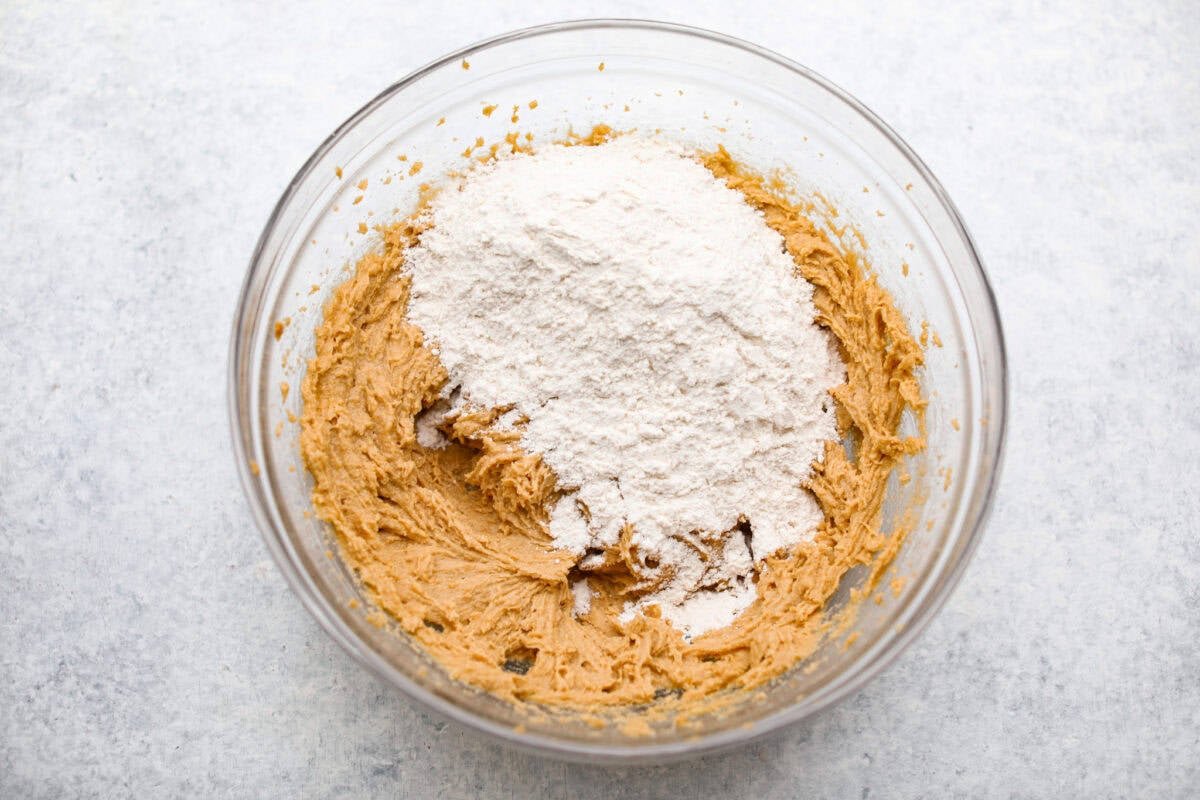 Peanut Butter Blossom Cookies are classic cookies that are perfect for every occasion. The delicious pairing of peanut butter and chocolate in these soft, buttery cookies will delight cookie lovers of all ages. Overhead shot of the wet ingredients with the dry ingredients dumped on top.
