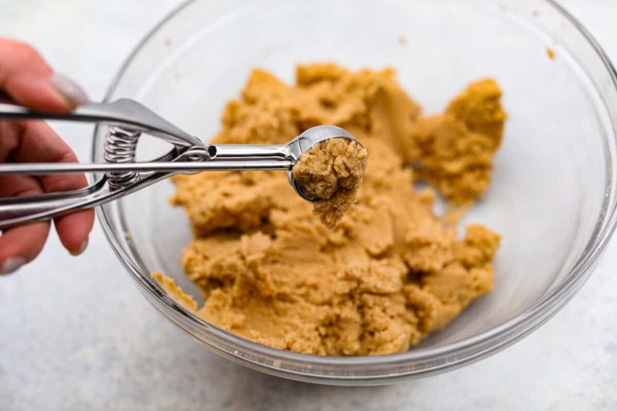 Peanut Butter Blossom Cookies are classic cookies that are perfect for every occasion. The delicious pairing of peanut butter and chocolate in these soft, buttery cookies will delight cookie lovers of all ages. Overhead shot of someone using a cookie scoop to scoop portions of dough.