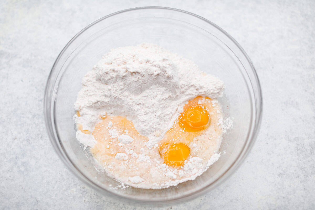 Strawberry Crinkle Cookies are the perfect blend of soft and chewy with a sweet, powdered sugar coating. Their vibrant color and classic strawberry cake flavor make them perfect for any occasion. Overhead shot of the cake mix, eggs, and butter in a mixing bowl.