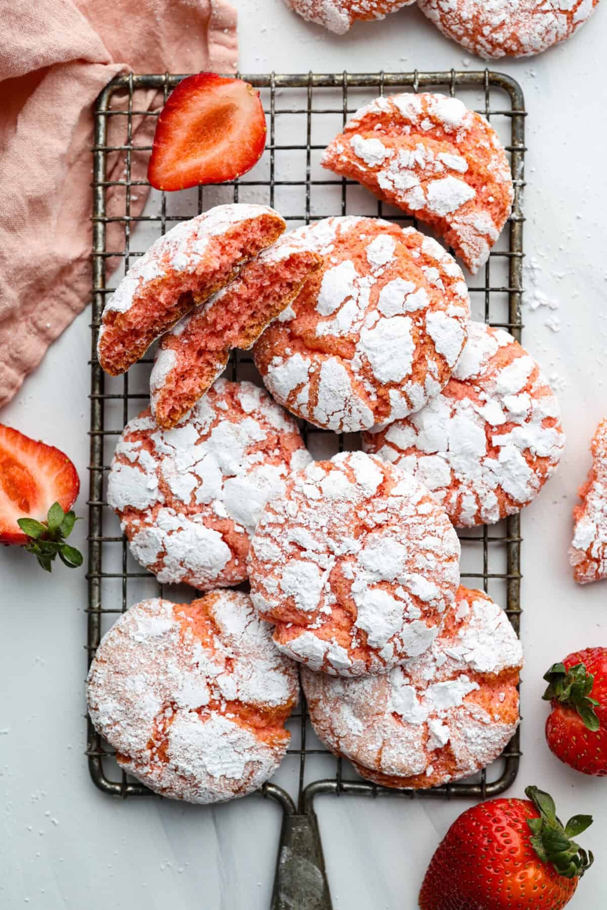 Strawberry Crinkle Cookies are the perfect blend of soft and chewy with a sweet, powdered sugar coating. Their vibrant color and classic strawberry cake flavor make them perfect for any occasion. Overhead shot of strawberry crinkle cookies stacked on a cooling rack.